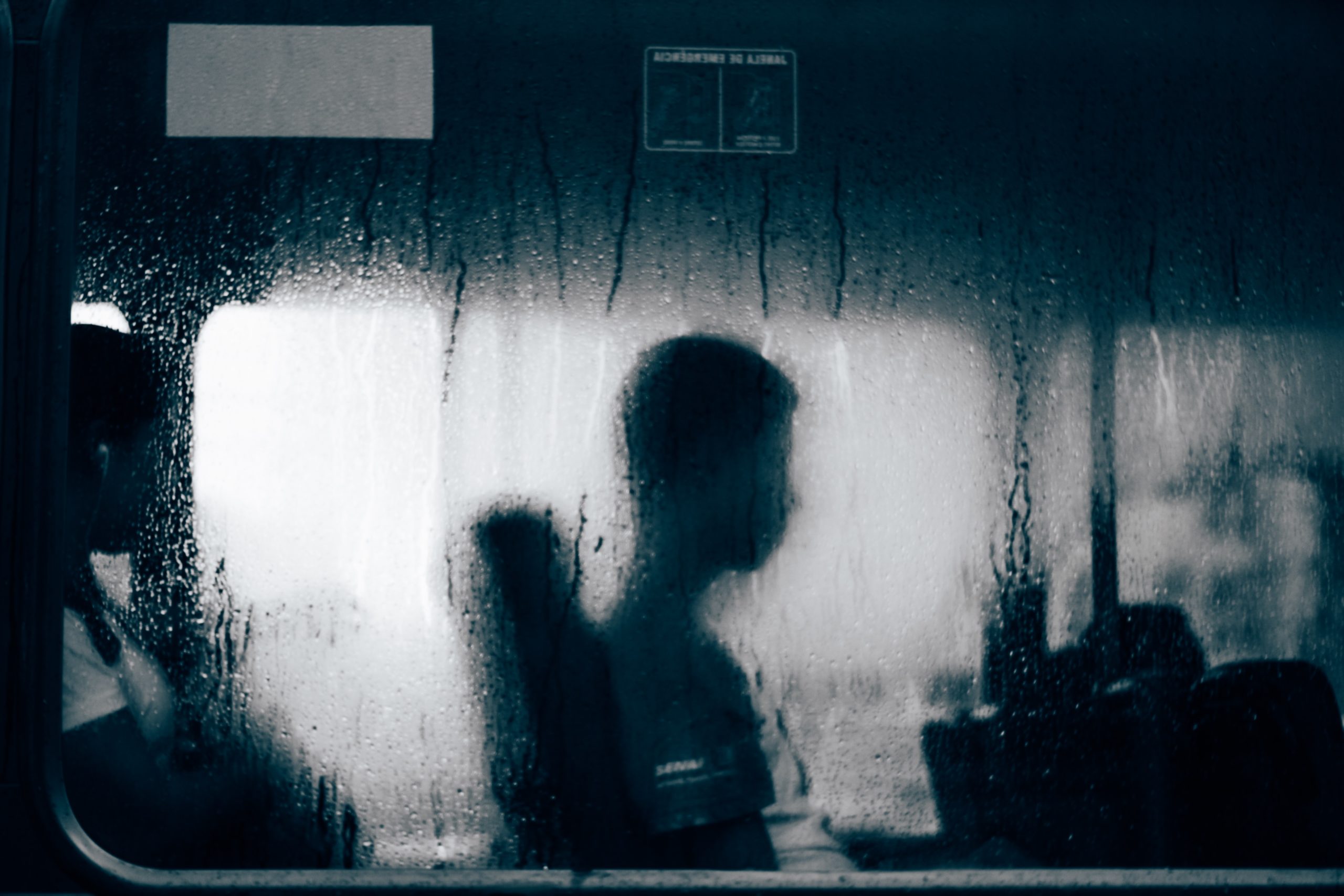 Ventana de un autobús con el cristal mojado por la lluvia, dentro se ve la silueta de un hombre sentado